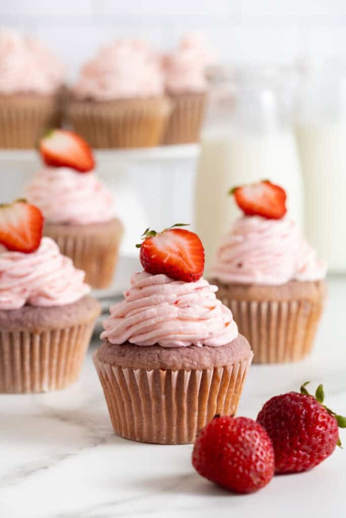 Several strawberry cupcakes on a white countertop with milk in background