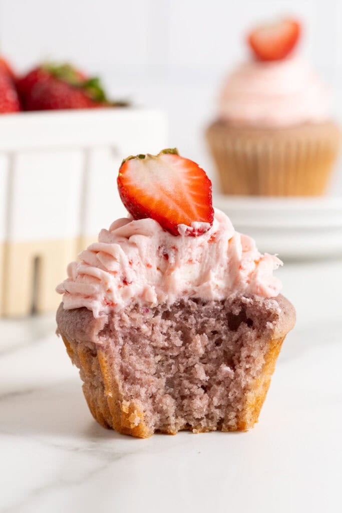 A close up of a strawberry cupcake that has been bitten into