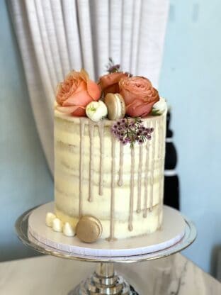 A deliciously tall vanilla cake with macaroons and flowers on it as decorations