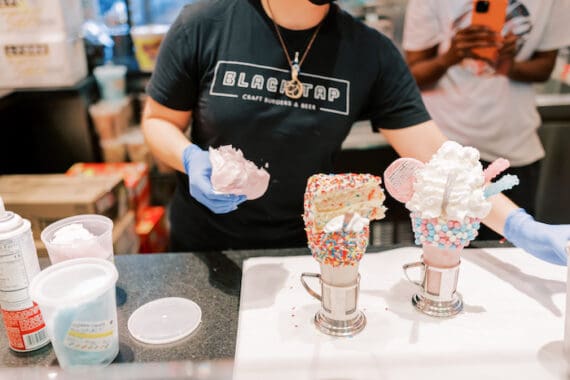 A woman at Black Tap restaurant making two milkshakes to serve