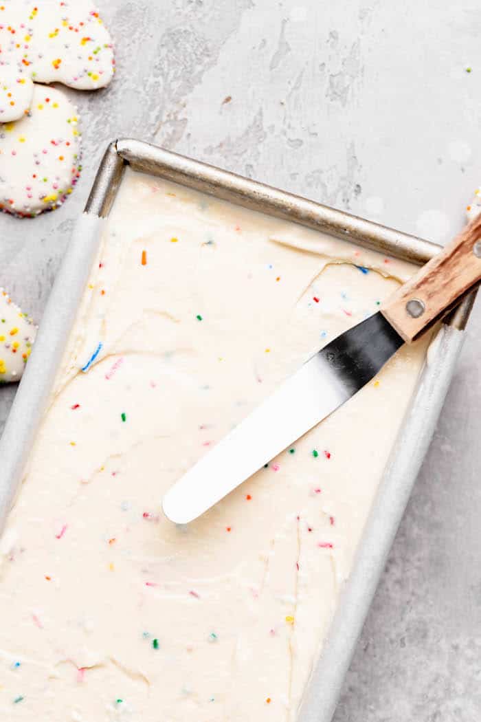 Ice cream being smoothed in cake pan with frosted cookies nearby