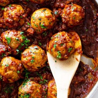 A close up of a pan of barbecue meatballs with a wooden spoon ready to serve