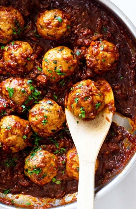 A close up of a pan of BBQ meatballs with a wooden spoon ready to serve