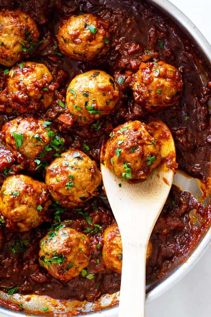 A close up of a pan of barbecue meatballs with a wooden spoon ready to serve