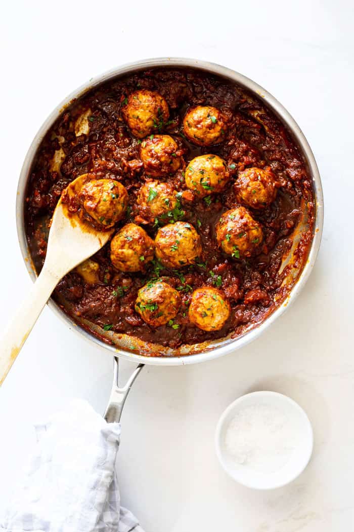 An overhead shot of a pan with bbq meatballs and a wooden spoon about to serve them