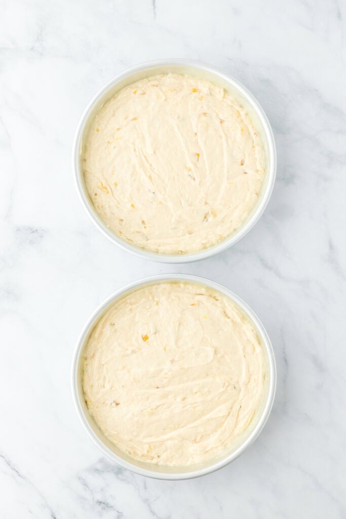 Banana cake batter added to two cake pans on white countertop before baking