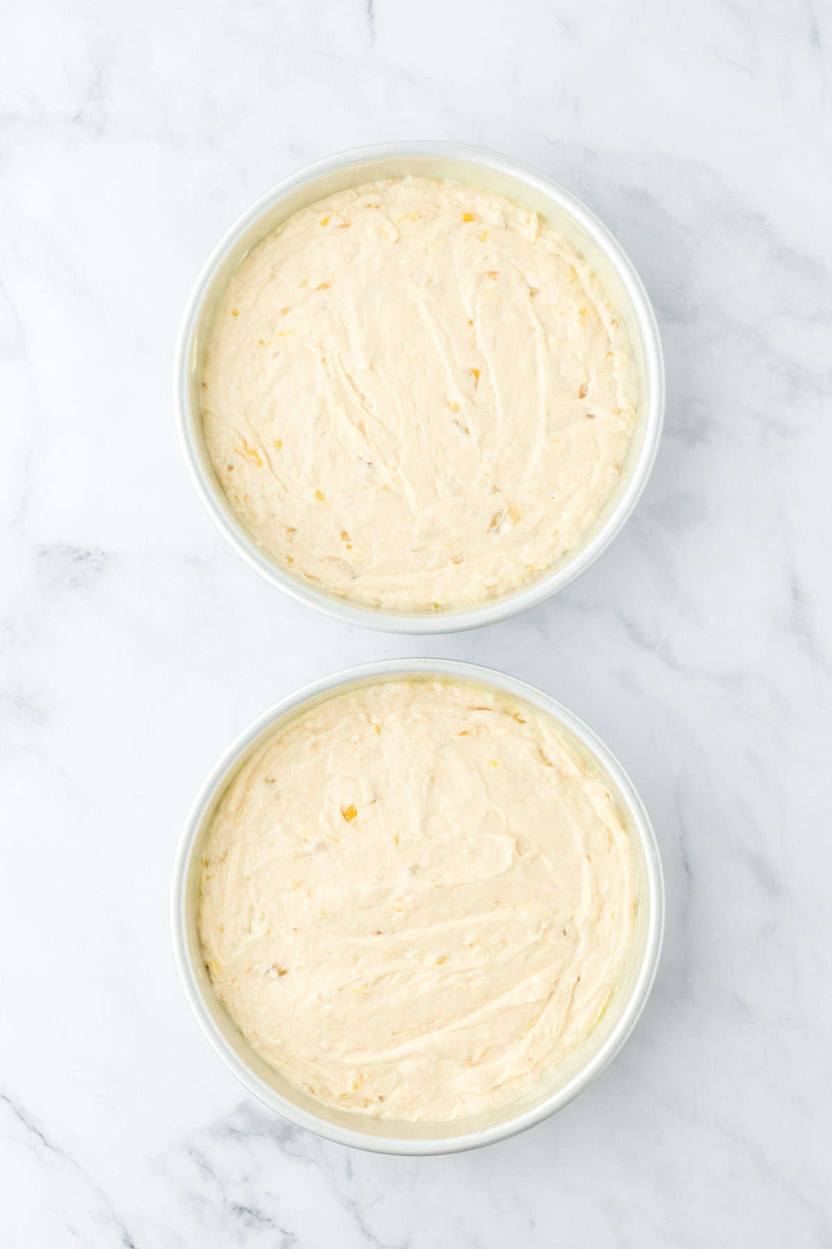 Banana cake batter added to two cake pans on white countertop before baking