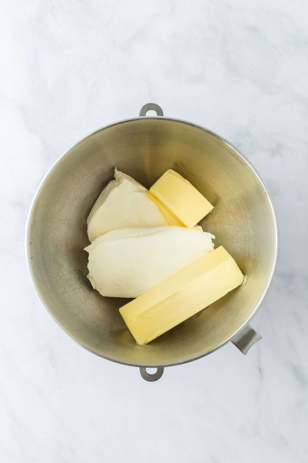 Cream cheese and butter added to a stand mixer bowl on white countertop