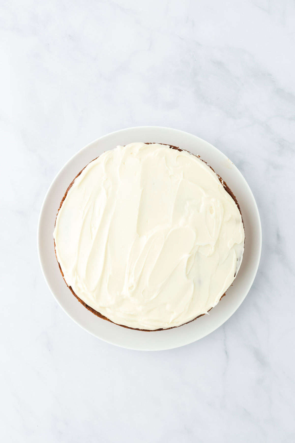 Cream cheese frosting on layer of banana cake on white countertop