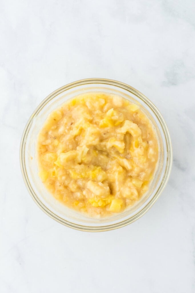 Stirred together banana and pineapple in a glass bowl on a white background