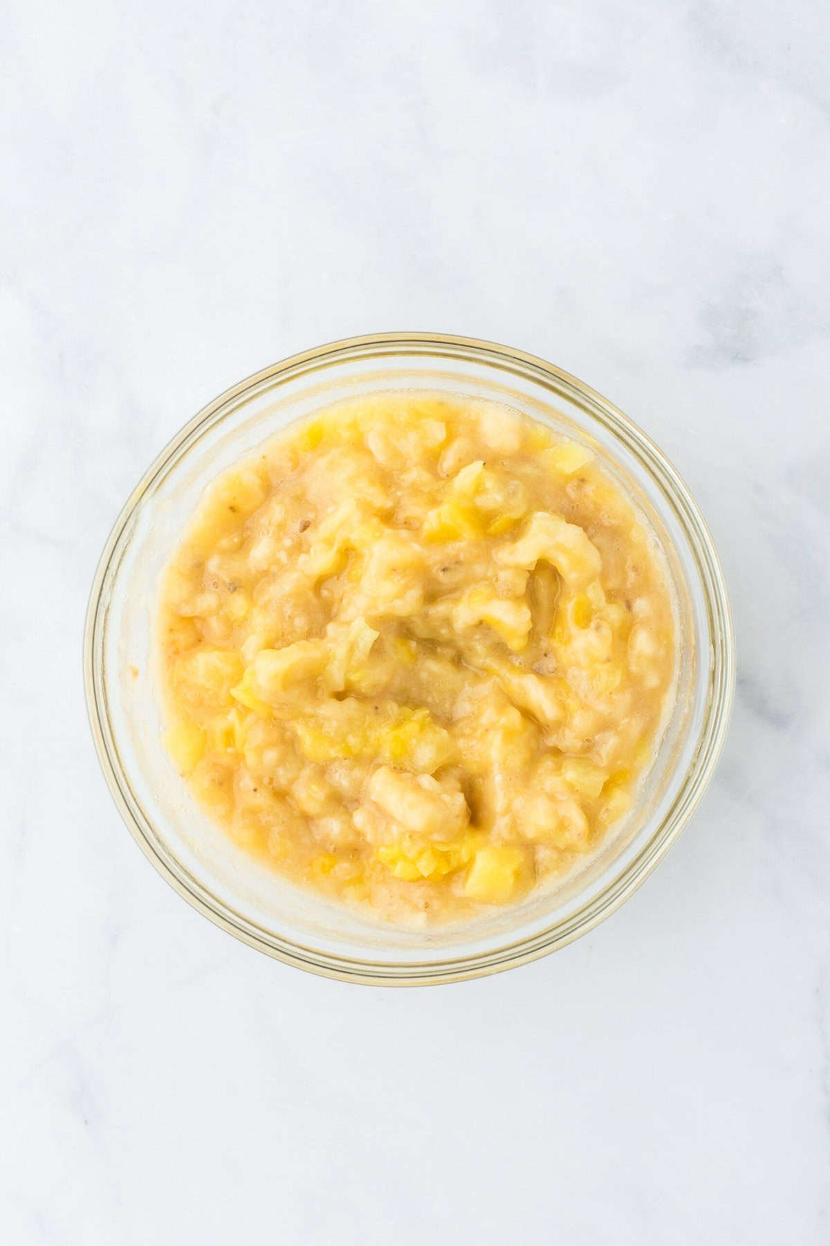 Stirred together banana and pineapple in a glass bowl on a white background