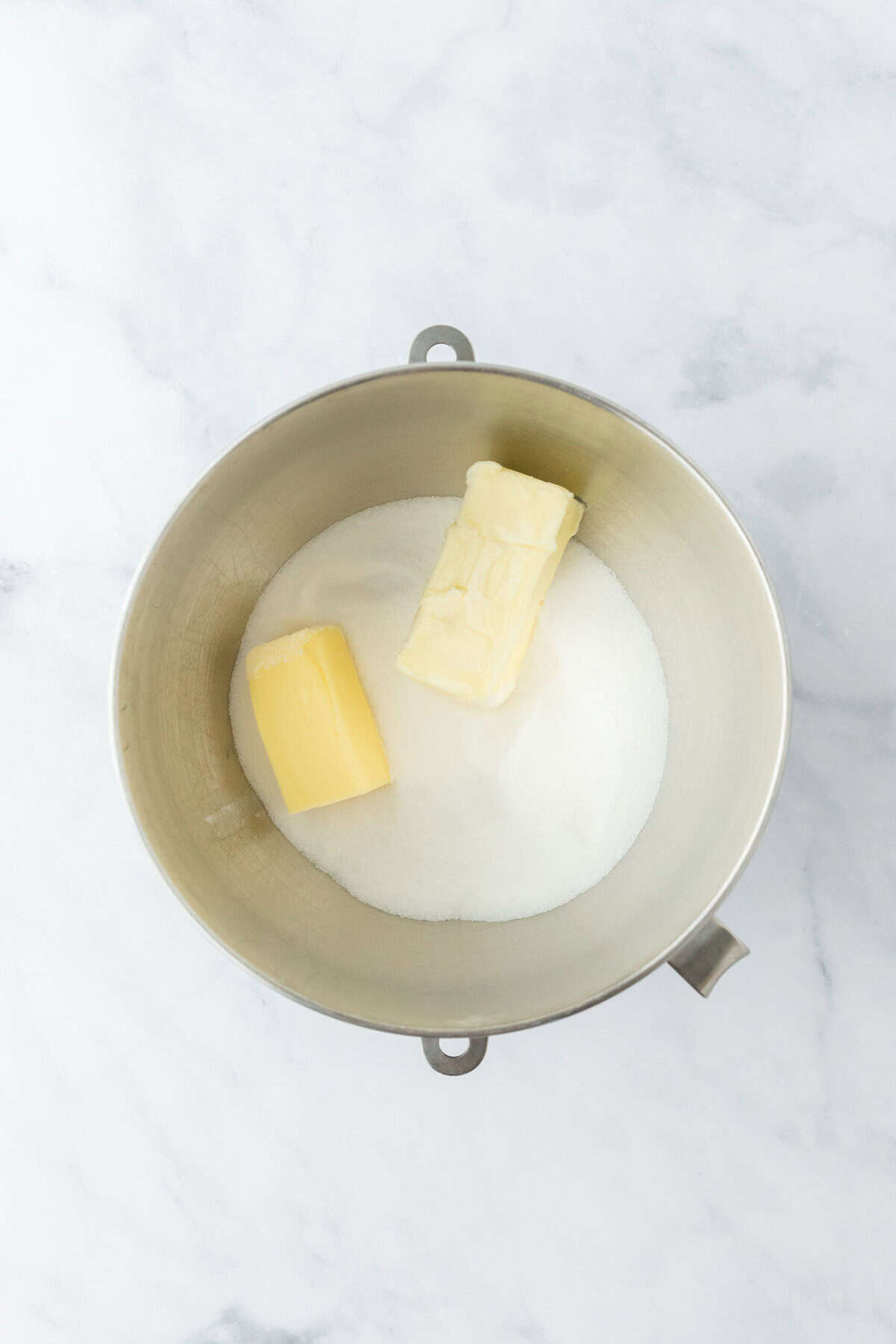 Butter and sugar in a stand mixer bowl on white countertop