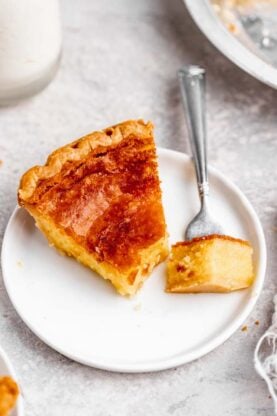 A slice of chess pie on a white plate with a piece being eaten