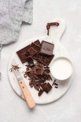 Chocolate squares, heavy cream and a knife against a white background