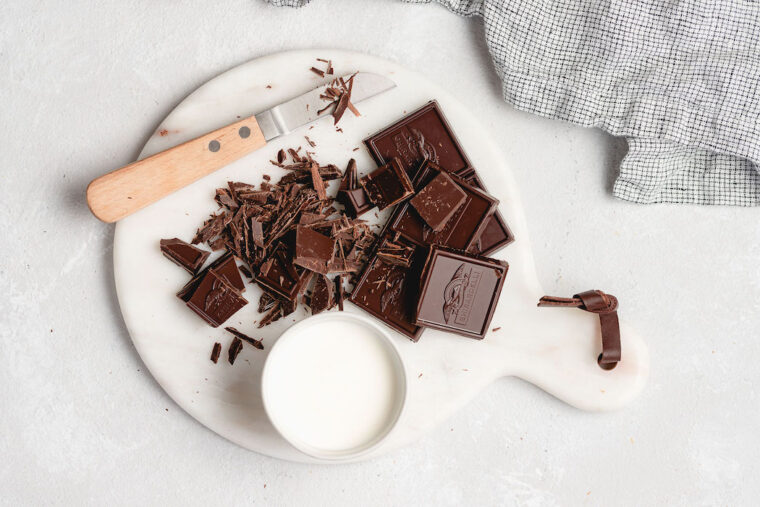 Chocolate squares, heavy cream and a knife against a white background