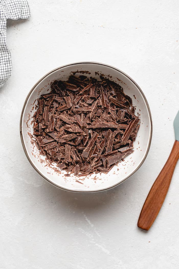 Chopped chocolate in a white bowl on white countertop