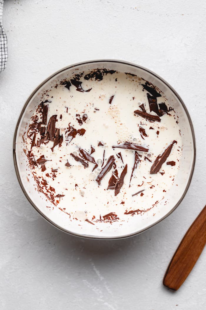 Shaved chocolate in a bowl of hot whipping cream on white background