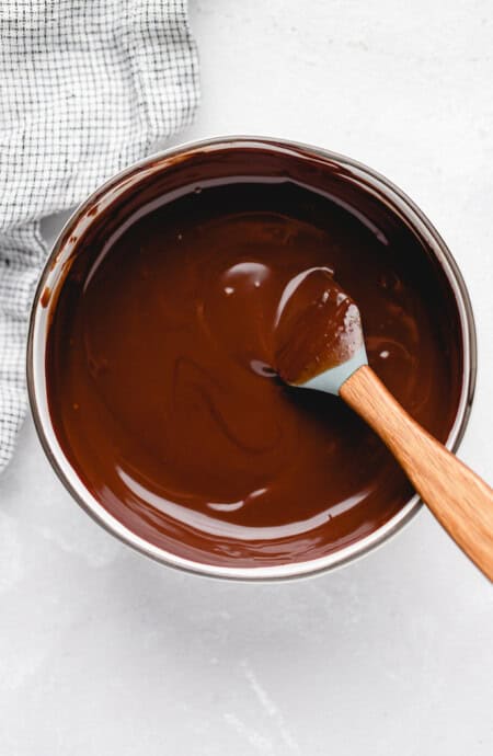 Chocolate ganache recipe being stirred slowly in a white pot with a spatula