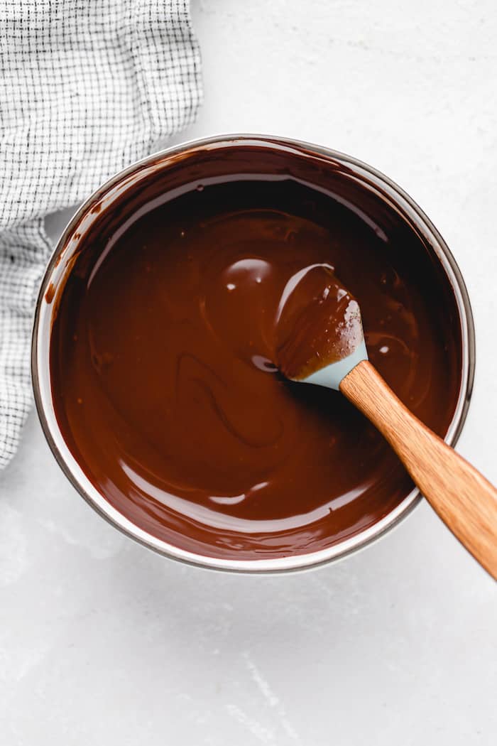 Chocolate ganache being stirred slowly in a white pot with a spatula