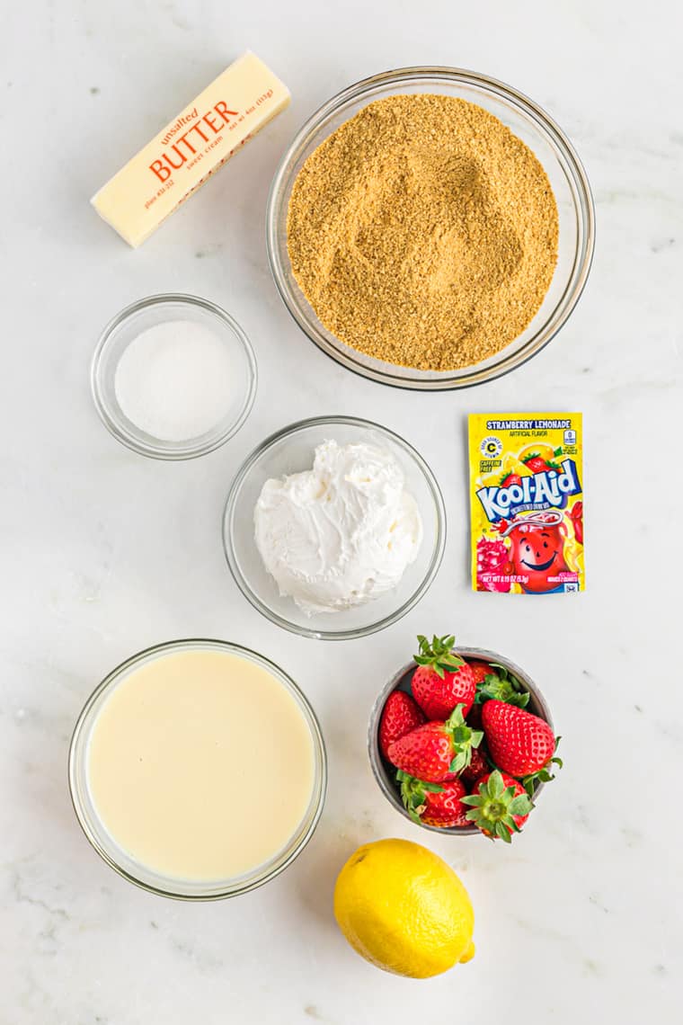 Bowls of ingredients such as graham cracker crumbs, butter, a kool-aid packet, strawberries and condensed sweetened milk