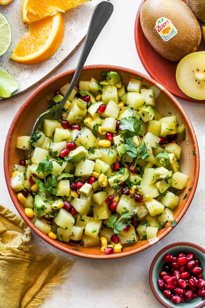 A kiwi salsa that is being stirred with a spoon with pomegranate