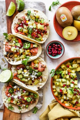 Salmon tacos with kiwi salsa layered next to each other with a bowl of salsa with pomegranate seeds in a small bowl