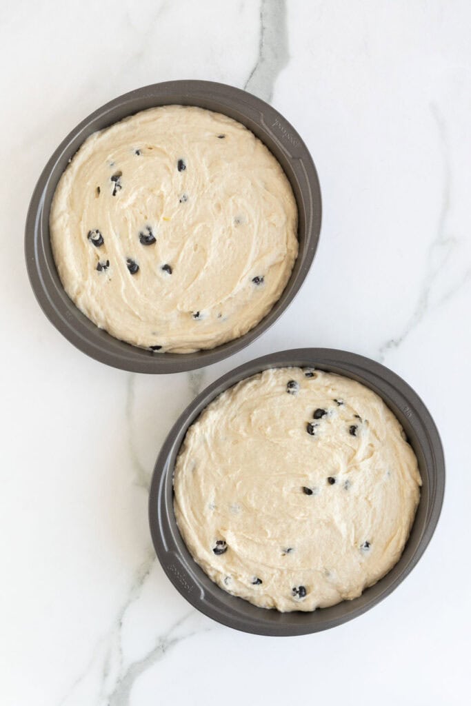 Two round cake pans filled with blueberry cake batter, ready for baking