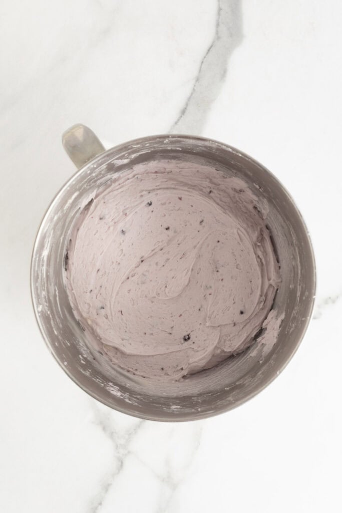 A metal mixing bowl with smooth, purple blueberry frosting