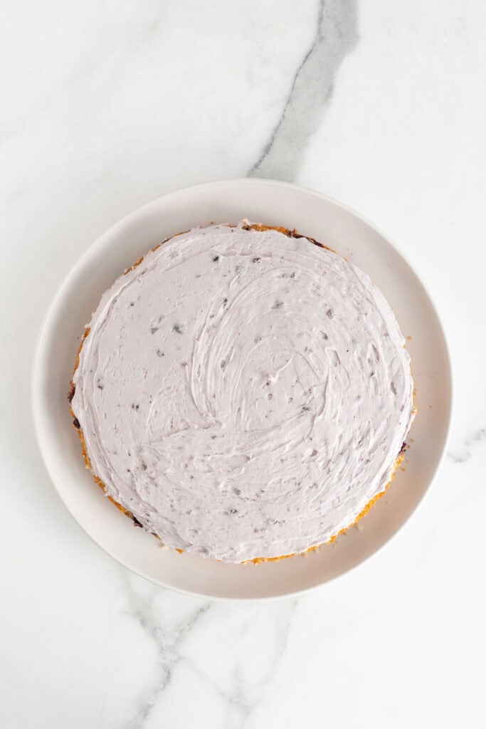 A cake layer on a plate, spread with blueberry frosting