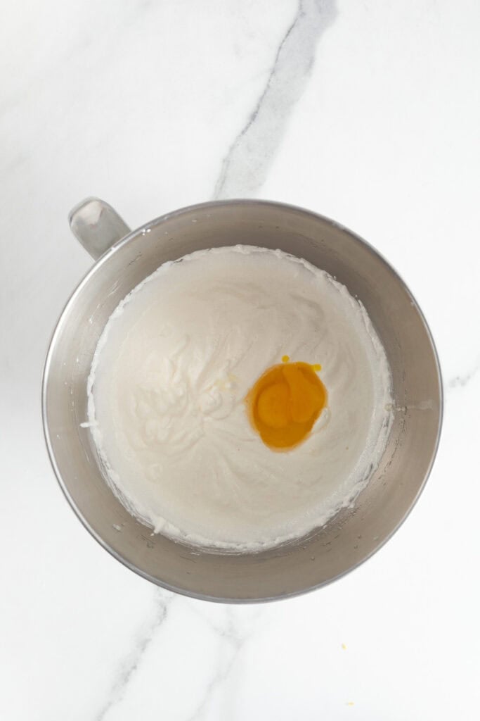 A metal mixing bowl with creamed butter and sugar, with a cracked egg on top
