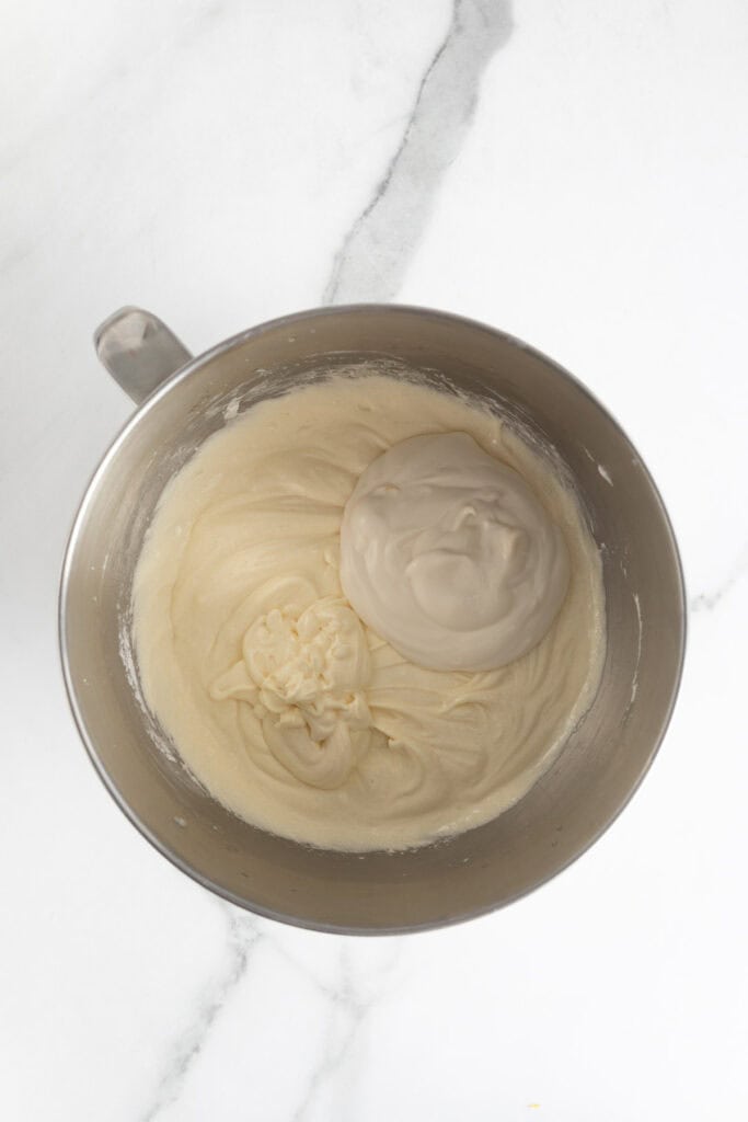 A metal mixing bowl with thick cake batter and sour cream mixture added on top