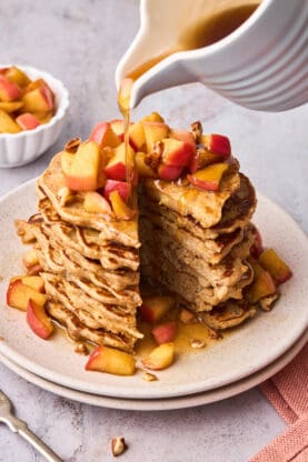 Apple cinnamon pancakes being drizzled with maple syrup 