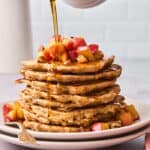 Maple syrup drizzling over a large stack of apple cinnamon pancakes ready to serve