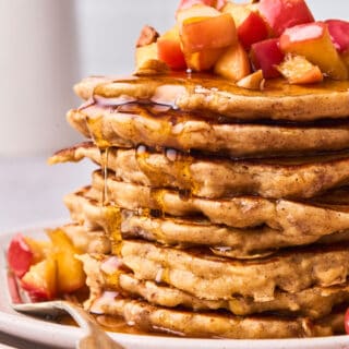 A close up of a large stack of apple cinnamon pancakes with syrup dripping down the sides