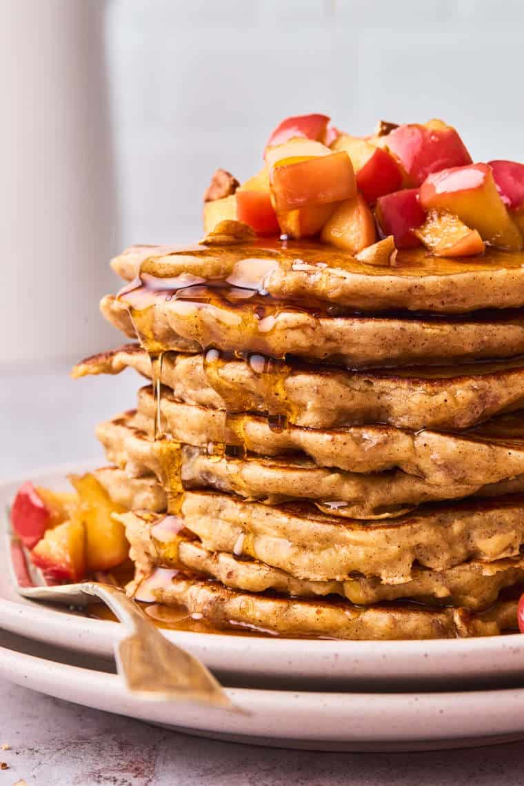 A close up of a large stack of apple cinnamon pancakes with syrup dripping down the sides