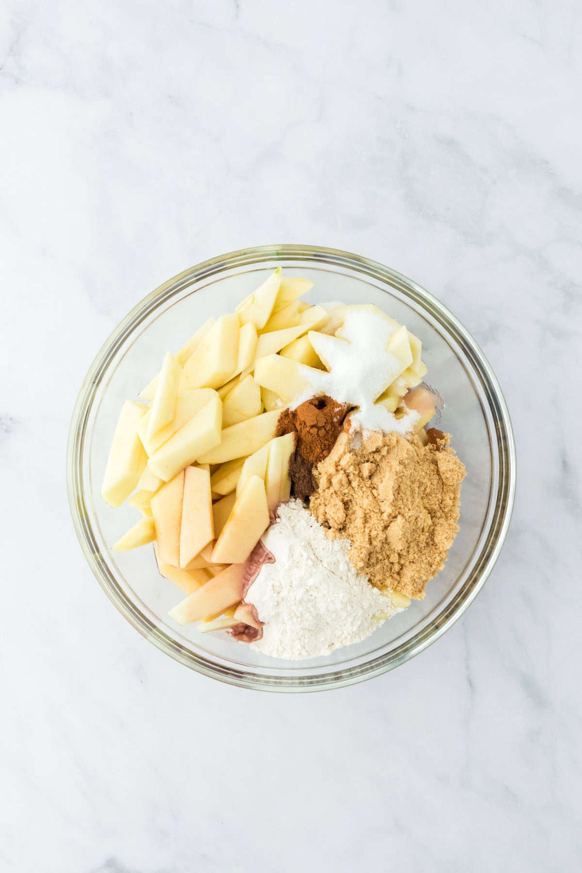 Apple slices, sugars and spices in clear bowl on white background