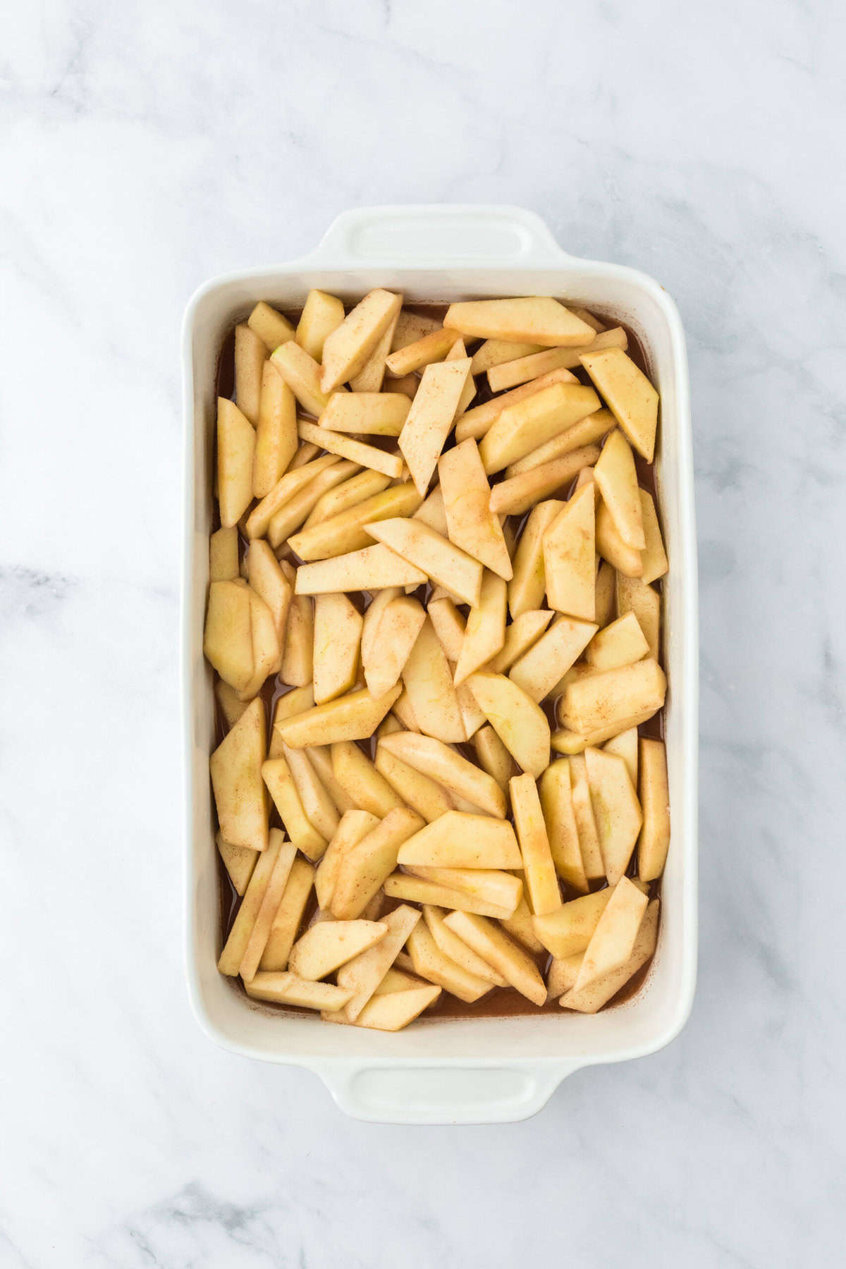 Apple slices in a white baking dish on white background