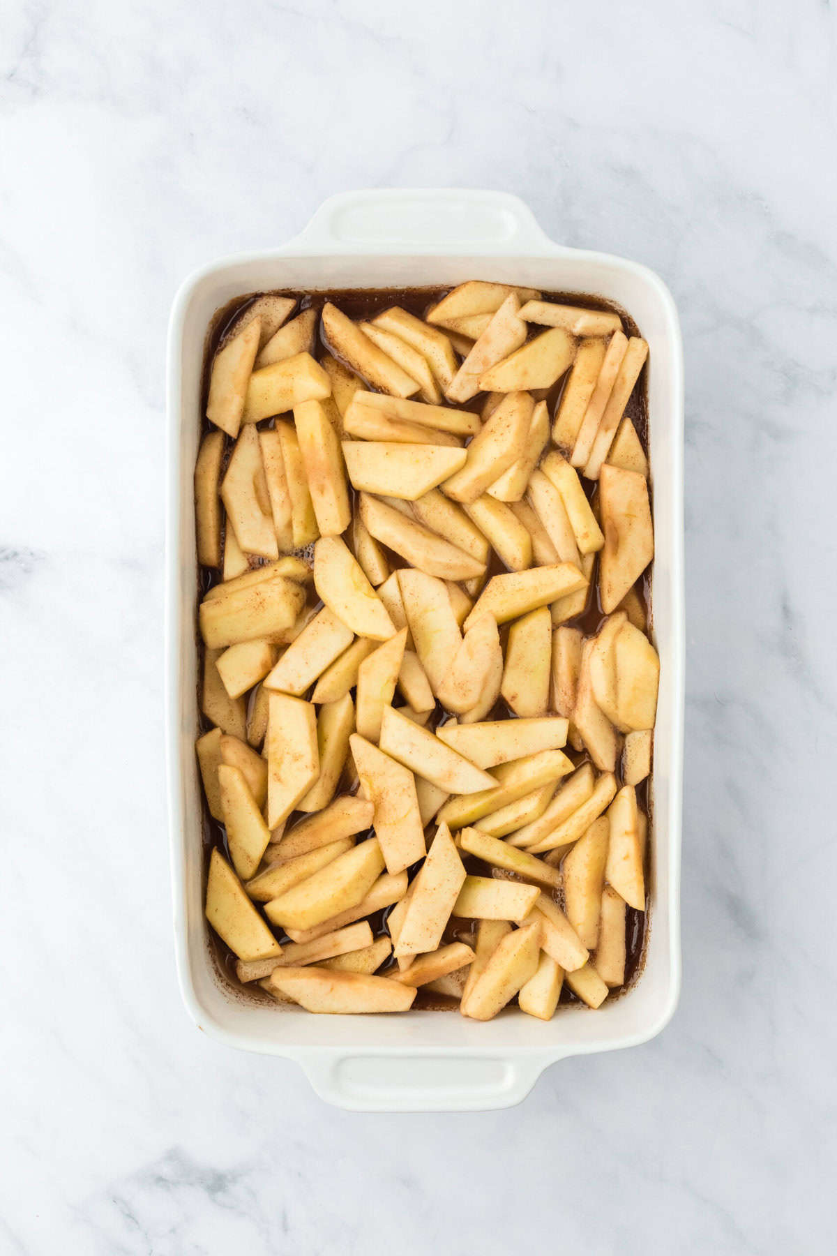 Tender apple slices in a white baking dish on white background.