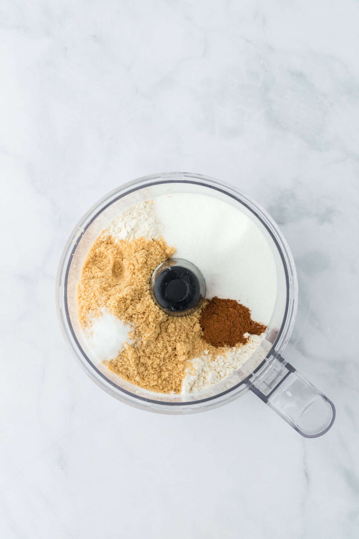 Dry ingredients in a food processor bowl before pulsing on white background