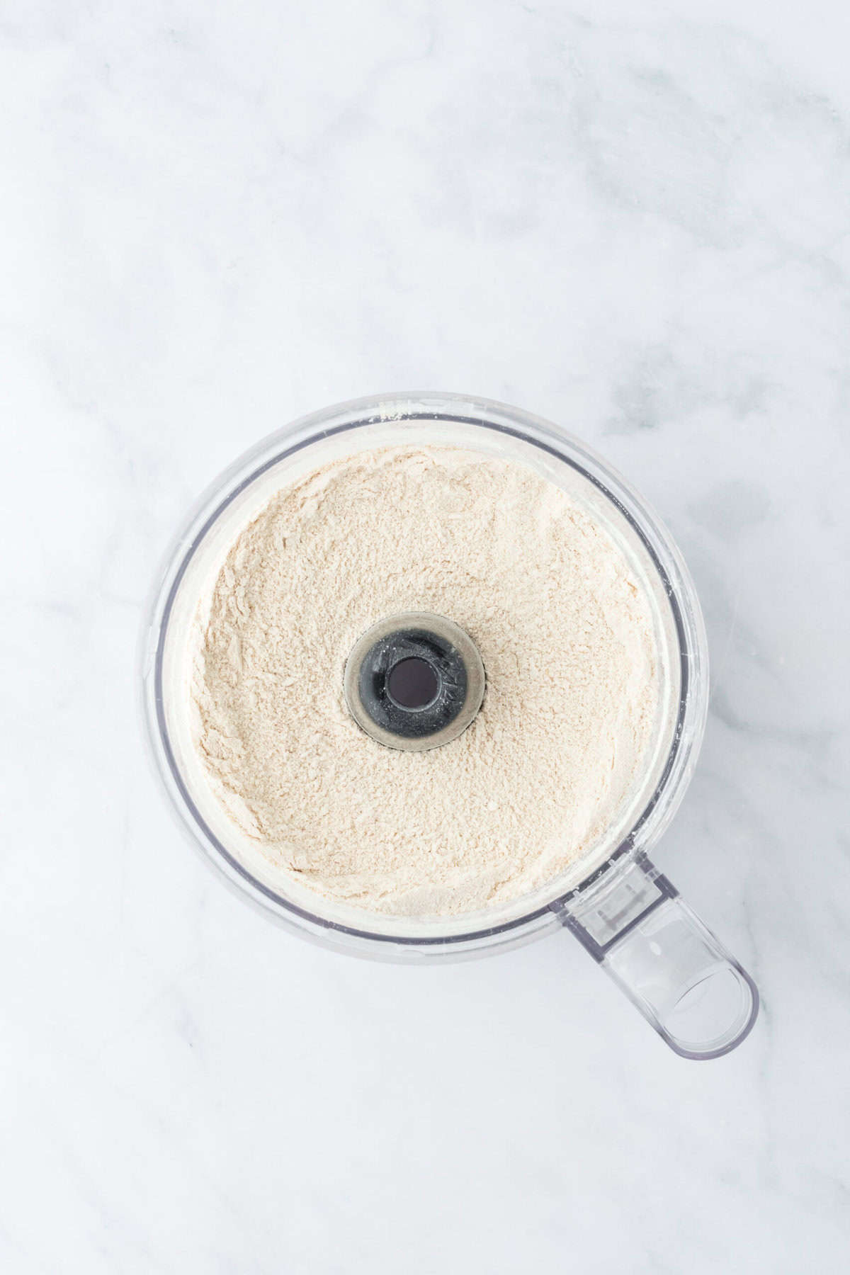 Pulsed biscuit dry ingredients in a food processor bowl on white background