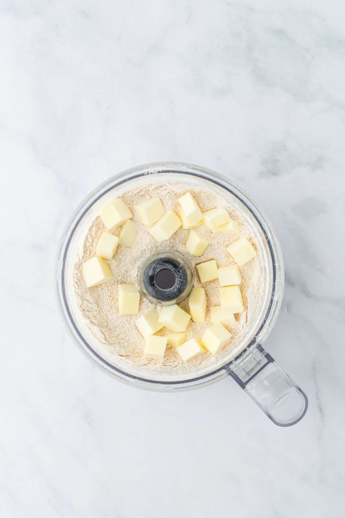 Cold butter added to food processor bowl and dry ingredients on white background