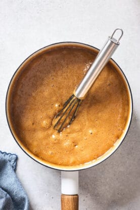 Caramel sauce bubbling on a white background with a silver whisk