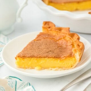 A slice of the best chess pie recipe on a white plate with striped napkin and full pie in white background