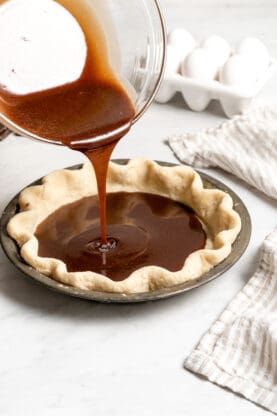 Chocolate pie filling being poured into a pie crust before baking
