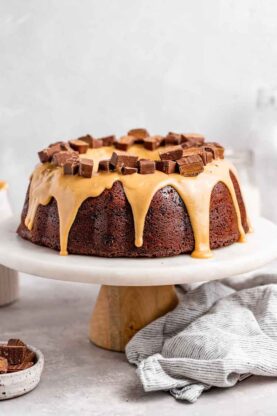 A delicious chocolate cake on a white cake stand with a caramelized white chocolate glaze