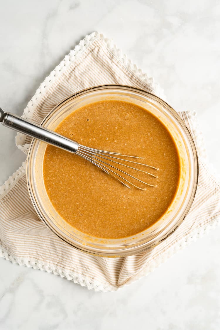 Pumpkin pie filling in a glass bowl with a whisk against white background and napkin