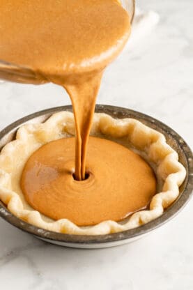 Pumpkin filling being poured into a prebaked pie crust