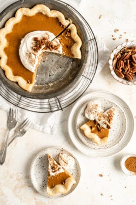 Slices of pumpkin pie on white plates with full pie in the background