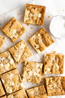 Brown butter blondies scattered against a white background with sea salt in a small bowl
