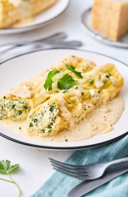 Two spinach manicotti on a white plate ready to serve